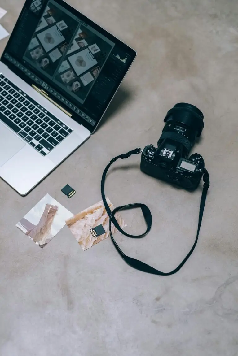 Overhead view of a camera and laptop with photos and memory cards on a marble surface.